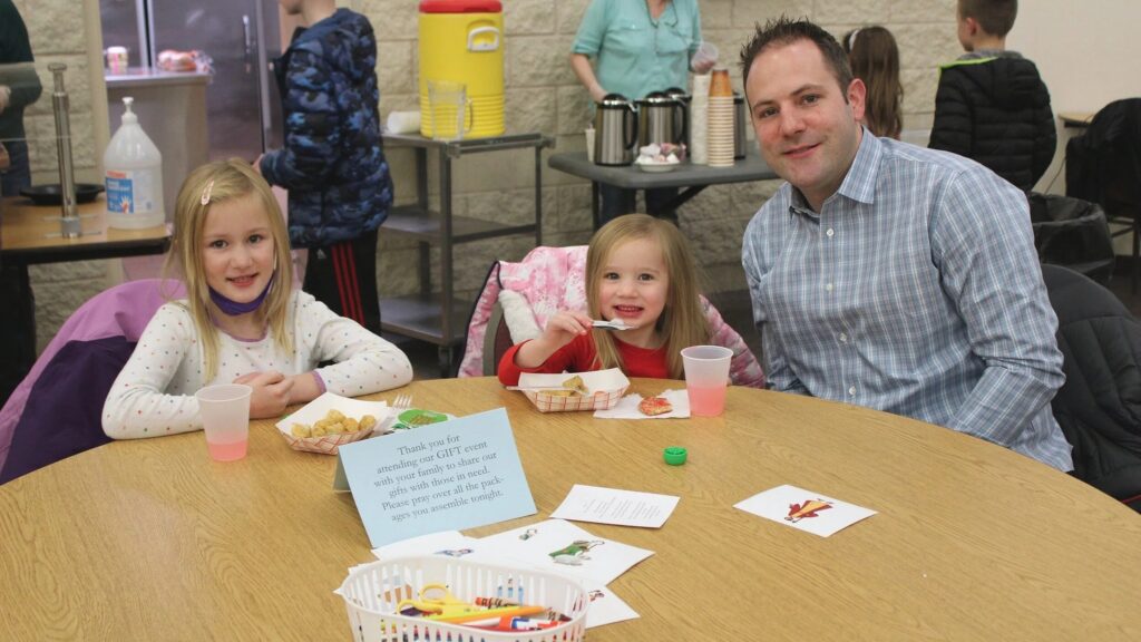 A family at a parish community event table with food and crafts