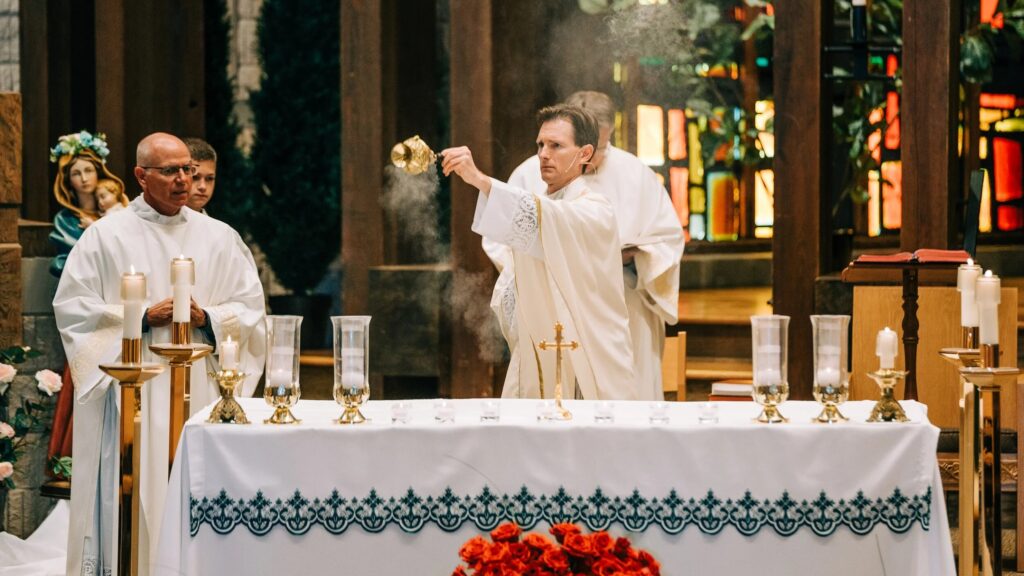 Priests conducting Catholic Mass at the altar with candles and stained glass windows